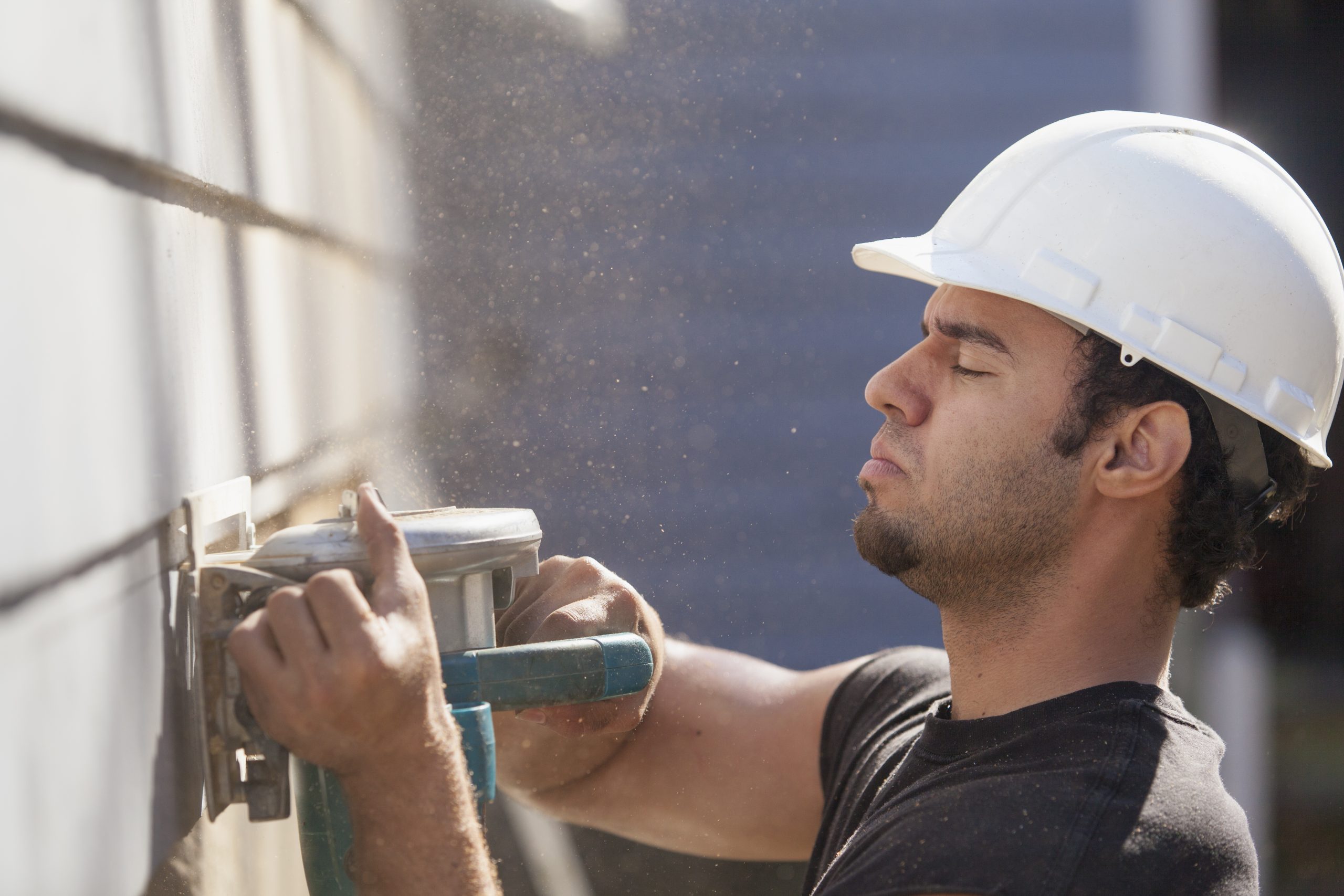 A man wearing a white helmet is working on siding with a tool